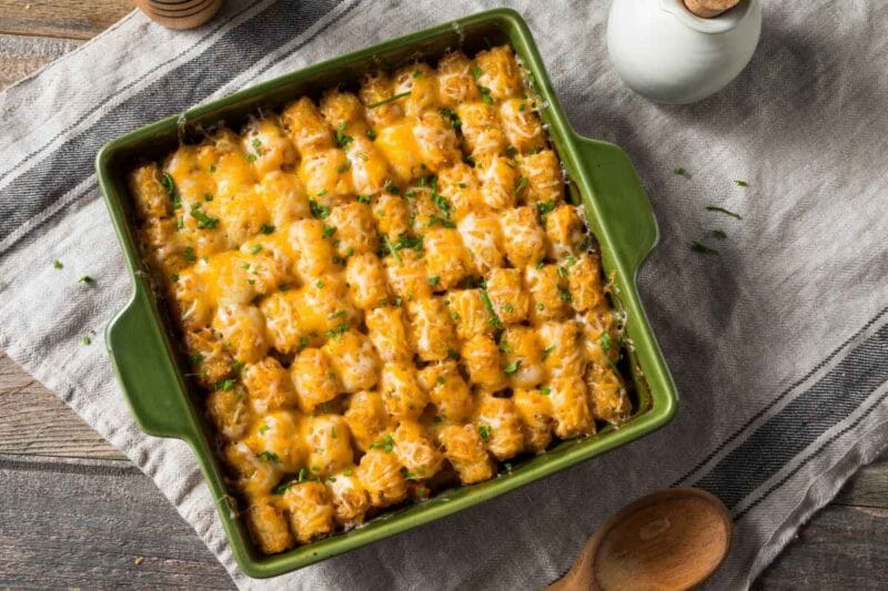 Top-down view of a baked Cheesy Tater Tot Casserole perfectly crisped and oozing with melted cheese, styled in a rustic kitchen setting with neutral linens.