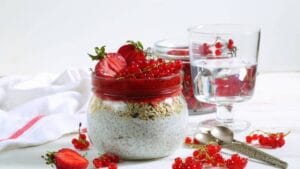 A jar of chia pudding topped with strawberry puree, granola, fresh strawberries, and red currants, served with a glass of water