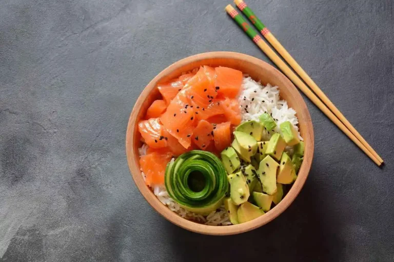 A vibrant poke bowl with fresh salmon, avocado, cucumber, and rice, garnished with black sesame seeds, served in a wooden bowl.