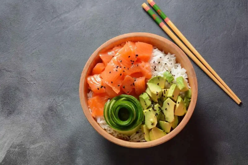 A vibrant poke bowl with fresh salmon, avocado, cucumber, and rice, garnished with black sesame seeds, served in a wooden bowl.