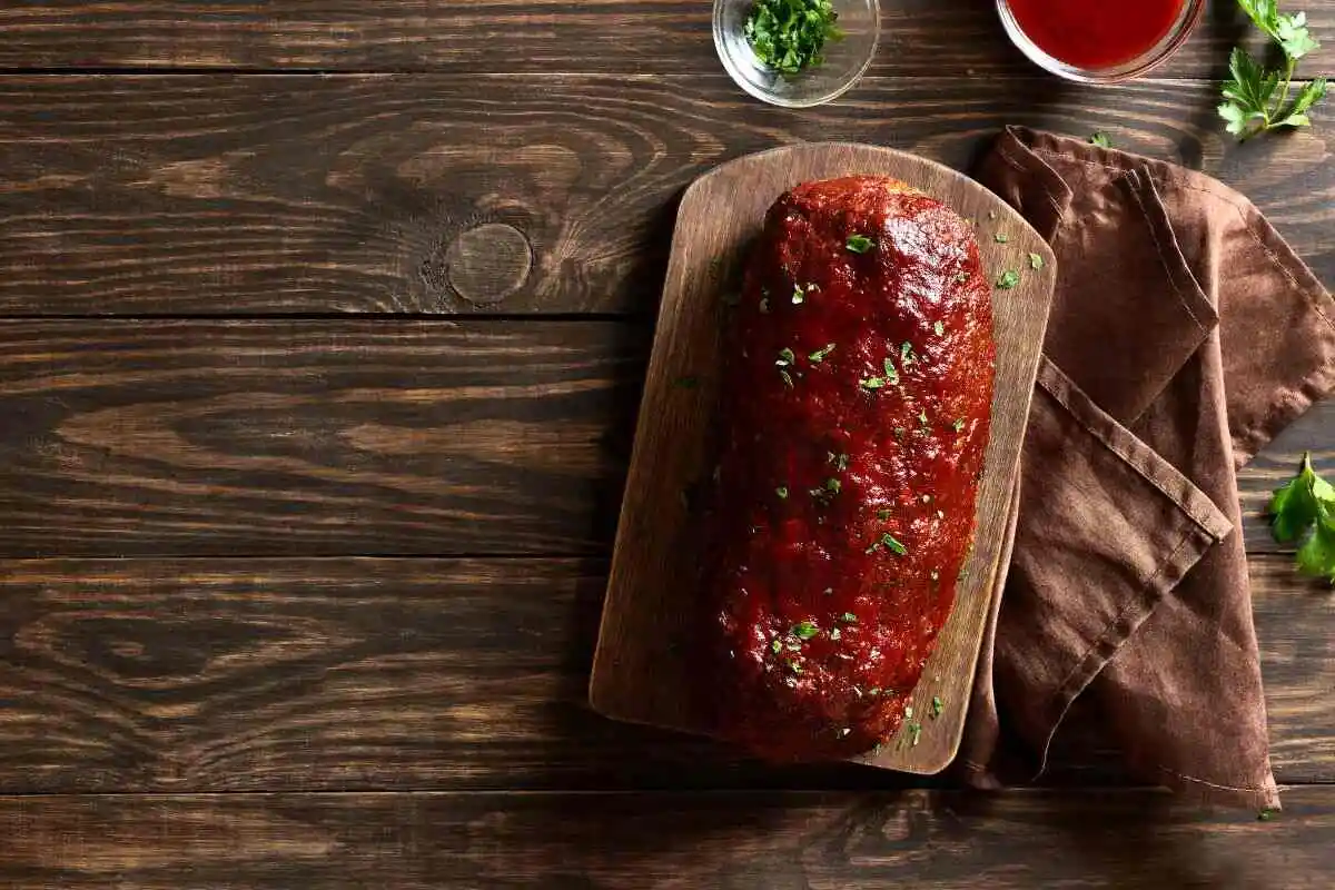A whole glazed meatloaf on a wooden board, garnished with fresh parsley, ready to be sliced and served for a comforting dinner.