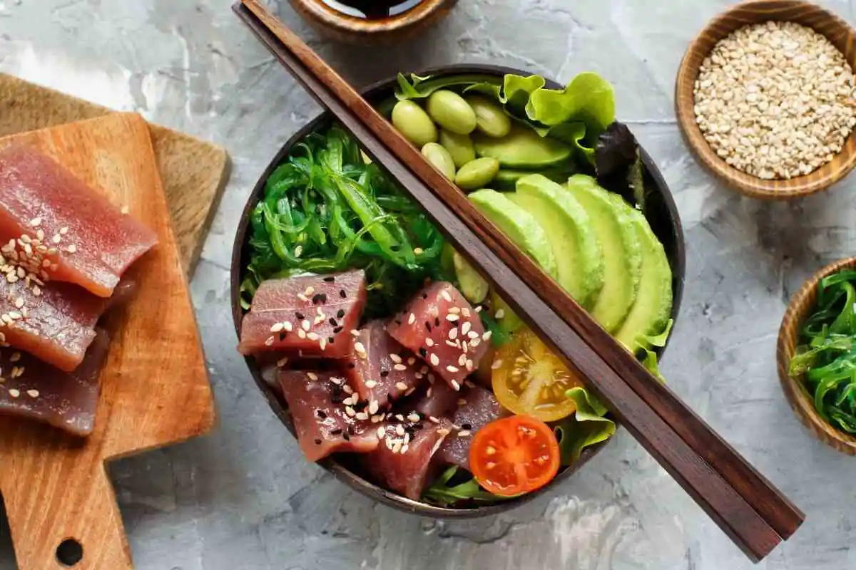 Are Poke Bowls Healthy? A fresh poke bowl featuring diced tuna, avocado slices, edamame, seaweed salad, cherry tomatoes, and sesame seeds, served with chopsticks.