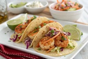 A plate of vibrant shrimp tacos with slaw, featuring tender, seasoned shrimp, crisp cabbage slaw, fresh cilantro, and lime wedges on soft tortillas.