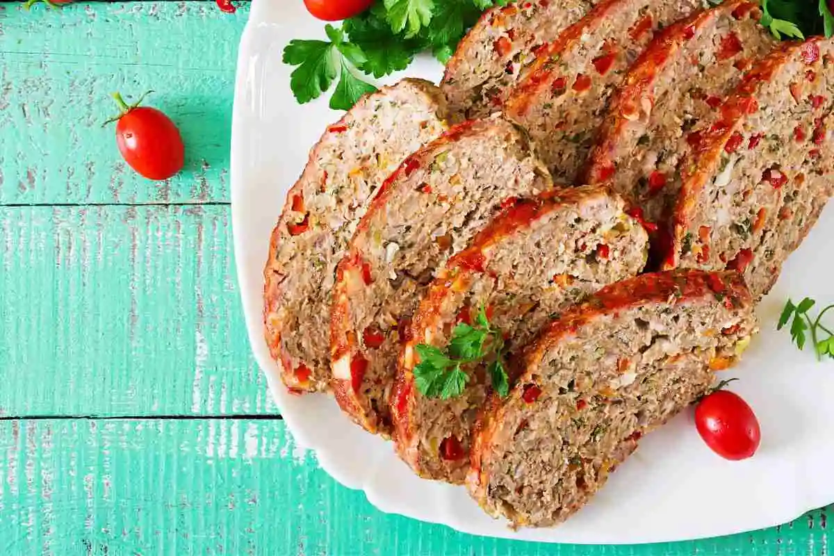 Sliced smoked meatloaf on a white platter, garnished with parsley and cherry tomatoes, perfect for a flavorful and hearty meal.