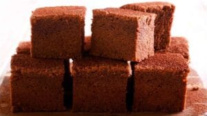 Close-up of stacked chocolate cake bars with a soft, moist texture, dusted with cocoa powder, displayed on a wooden surface, perfect for a sweet indulgence.