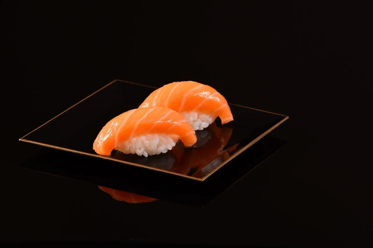 Two pieces of salmon nigiri sushi, artistically displayed on a sleek black plate with a subtle golden edge, reflecting a minimalist and modern aesthetic.