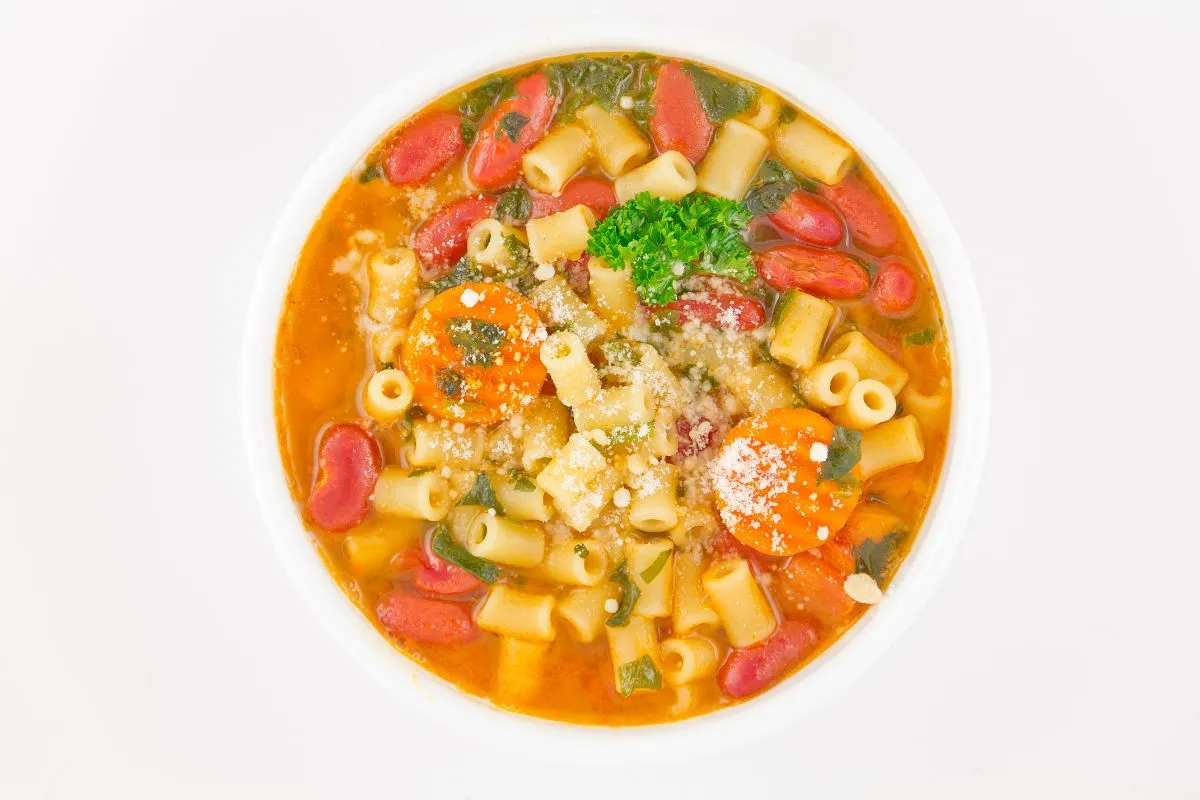 A colorful bowl of pasta e fagioli soup, featuring ditalini pasta, kidney beans, carrots, and a rich tomato broth garnished with parsley and Parmesan cheese, captured from an overhead view.