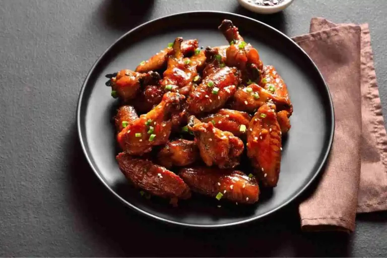 Smoked chicken wings glazed with a shiny sauce, garnished with green onions and sesame seeds, served on a black plate.