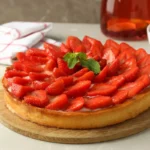 Whole strawberry cheesecake with a layer of fresh strawberries arranged on top, garnished with mint.