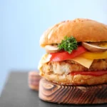 A turkey burger with cheddar cheese, tomato, lettuce, and parsley, served on a wooden plate.