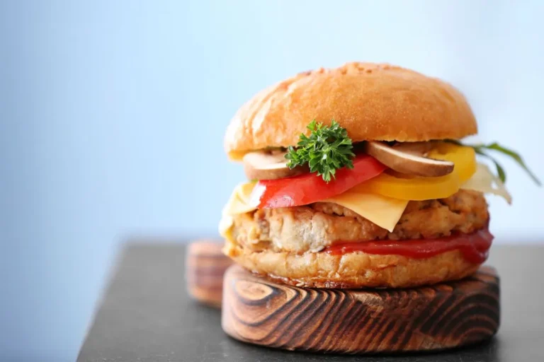 A turkey burger with cheddar cheese, tomato, lettuce, and parsley, served on a wooden plate.