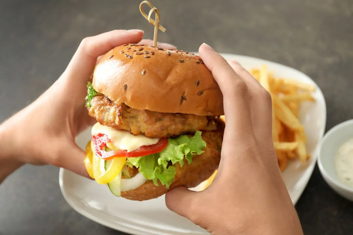 Hands holding a turkey burger loaded with lettuce, tomato, and cheese, served with fries on the side.