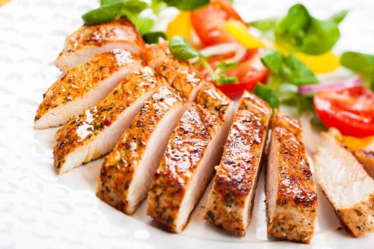 Is a Turkey a Type of Chicken? Sliced grilled chicken breast served with a fresh salad of tomatoes and greens, displayed on a decorative white plate.